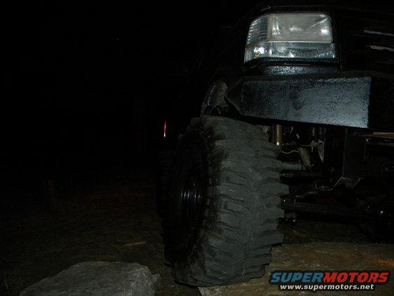 Black SUV's large front tire and headlight at night