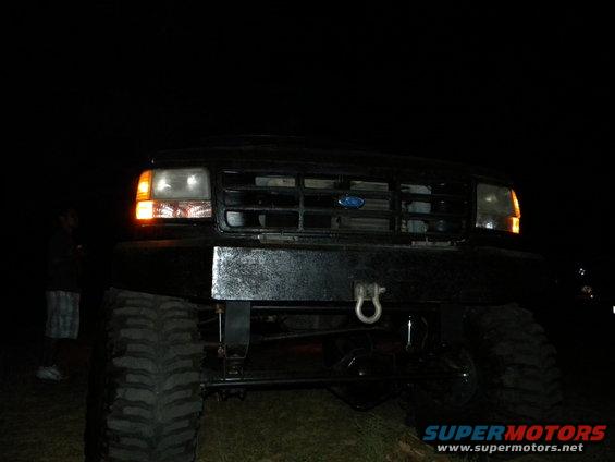 Front view of a black Ford F-Series truck with a custom bumper and large tires at night