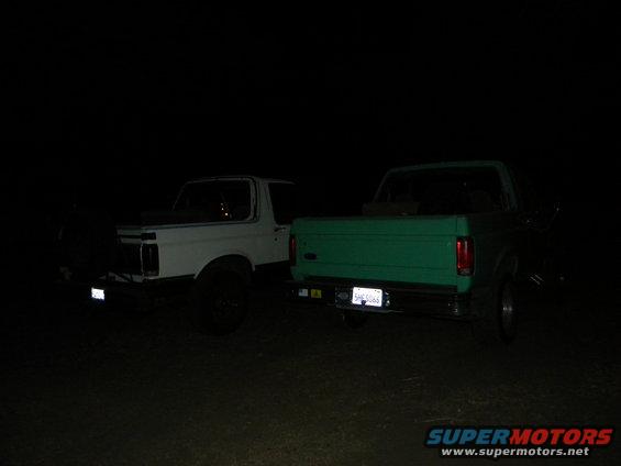 White 1992 Ford Bronco and green pickup truck parked at night