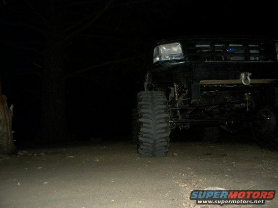 Front view of a black lifted Ford truck at night. It has large tires and a winch hook on the front bumper