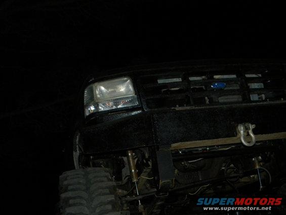 Front of a black Ford truck with a custom bumper and large tires. The grille has a blue Ford logo