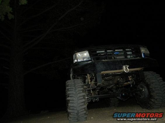 Black lifted Ford truck with large tires, front view, at night