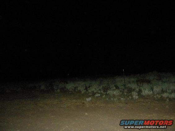 dark landscape with grass and fence posts at night, SUPERMOTORS.NET logo in corner
