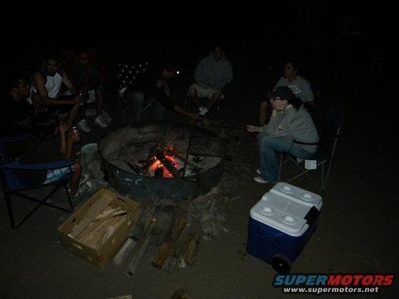 Dark scene with people gathered around objects, possibly a campfire