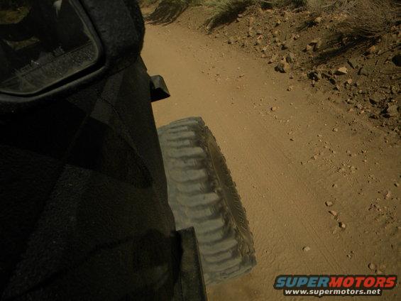 Side view of a vehicle's tire and fender on a dirt road