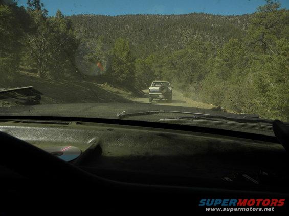 White pickup truck driving on a dirt road through trees