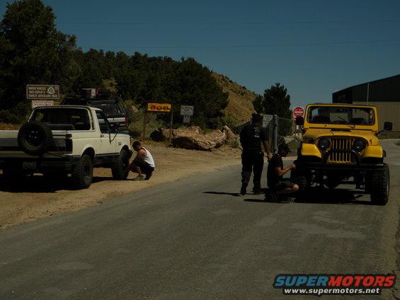 White pickup truck and yellow Jeep on a road, people working on tires