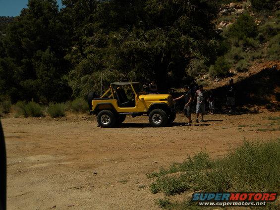 Yellow Jeep CJ-5 parked on dirt road with people nearby