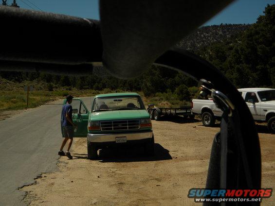 Green Ford F-150 pickup truck with driver's door open, parked on dirt lot next to a white Ford pickup