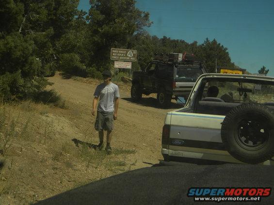 White 1992 Ford Bronco rear view with spare tire, black SUV behind
