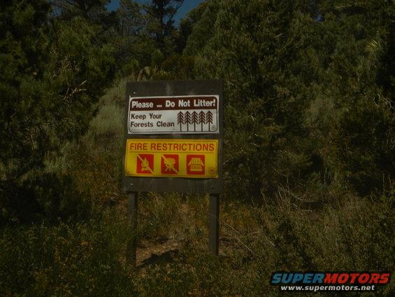 Wooden sign with "Please... Do Not Litter! Keep Your Forests Clean" and "FIRE RESTRICTIONS" with prohibition symbols