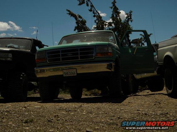 Green 1992 Ford Bronco with door open, parked next to a black truck