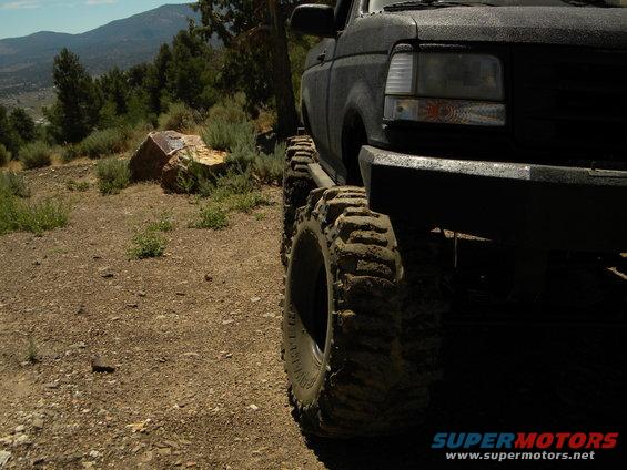 1992 Ford Bronco with large off-road tires on a dirt path, mountains in background