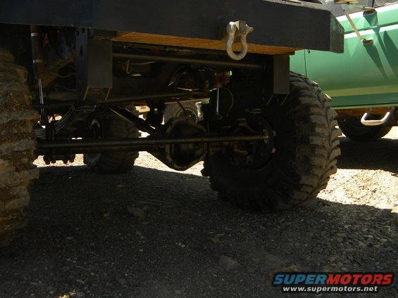 1992 Ford Bronco rear axle, suspension, and large tire, with a green vehicle in the background