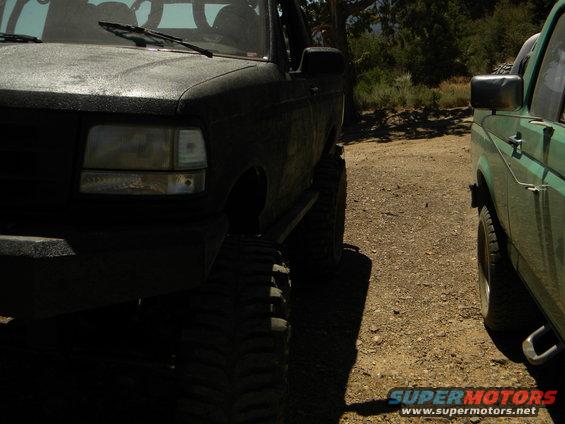 1992 Ford Bronco front quarter panel and lifted tire next to a green SUV