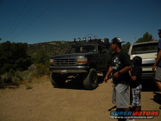 Black 1992 Ford Bronco with roof rack and off-road tires, parked on dirt road