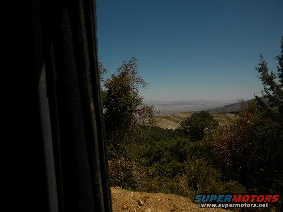 View from a vehicle of a dry, hilly landscape under a clear blue sky