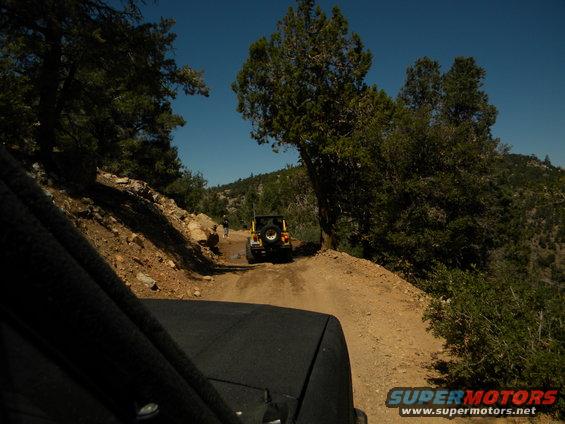 View from inside a vehicle looking at two Jeeps driving on a dusty mountain road