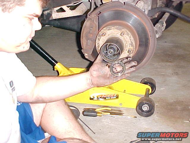Man holding a disassembled wheel hub assembly with a brake rotor and caliper visible