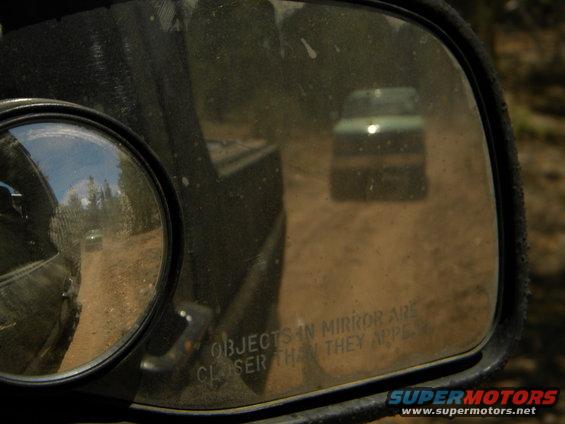 Green SUV reflected in side mirror on a dirt road