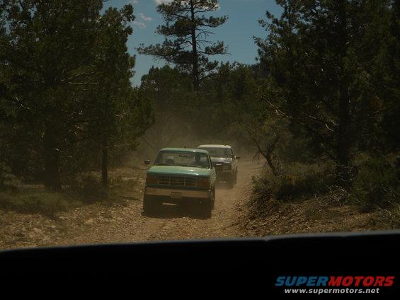 1992 Ford Bronco and another truck on a dusty dirt road