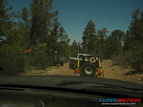 1992 Ford Bronco, white and yellow, with spare tire on rear, driving on dirt road with another SUV