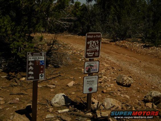 Trail signs indicating 'To John Bull Into' and 'Adopt-a-Trail National Forest'. One sign says 'Adopted by So Cal Broncos'