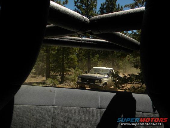 1992 Ford F-150 pickup truck, two-tone blue and white, driving on a dirt road in a forest