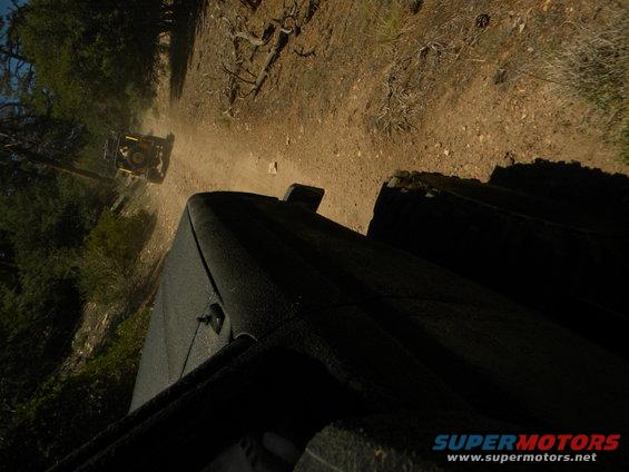 Yellow off-road vehicle kicking up dust on a dirt road, viewed from another vehicle