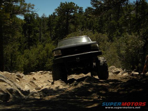 Black 1992 Ford Bronco with large tires navigating a rocky off-road trail