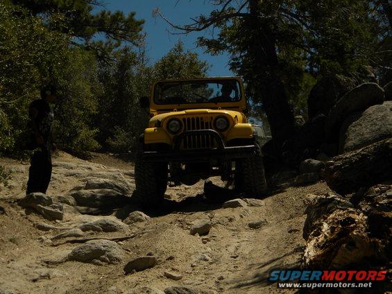 Yellow Jeep CJ-7 on a rocky trail, front view. Off-road tires, black grille guard
