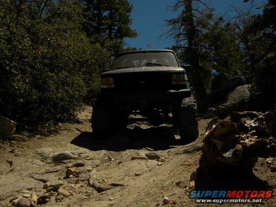 Black SUV with large tires driving on a rocky, wooded trail