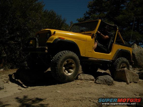 Yellow Jeep CJ navigating rocky terrain