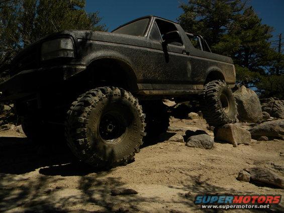 Black Ford Bronco with large off-road tires climbing over rocks