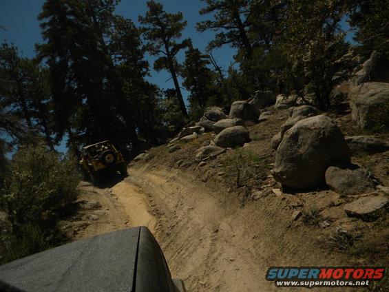 Yellow off-road vehicle on a dirt trail with trees and rocks