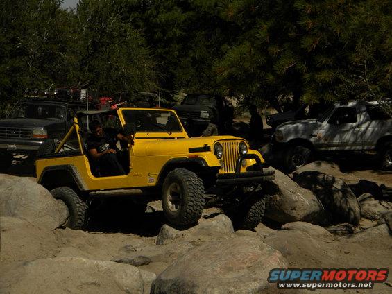 Yellow Jeep CJ-7 navigating rocks, with other off-road vehicles in the background