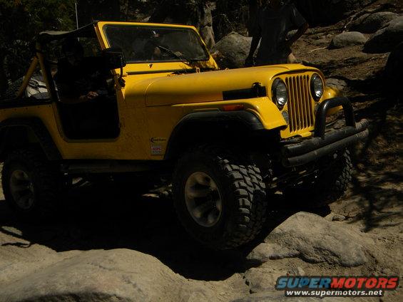 Yellow Jeep CJ-7 with soft top, off-roading on rocks. Visible text: SUPERMOTORS