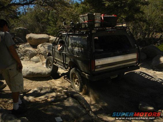 1992 Ford Bronco navigating a rocky trail with a roof rack loaded with gear