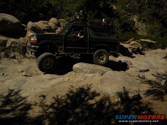 Black 1992 Ford Bronco off-roading over rocks, lifted suspension, roof rack