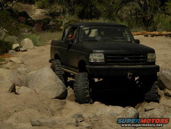 Black 1992 Ford Bronco with lifted suspension and large tires navigating rocky terrain