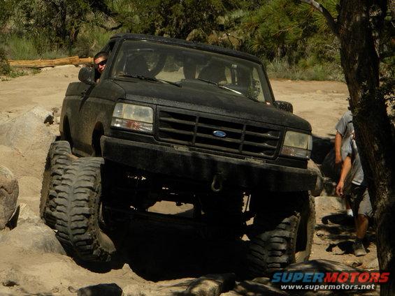 Black Ford Bronco climbing over rocks on a dirt trail. Driver is visible