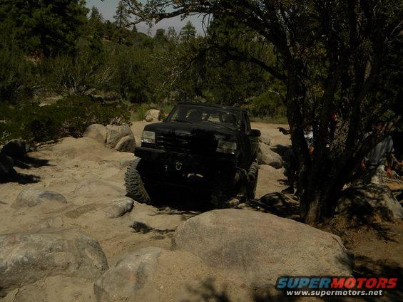 Black 1992 Ford Bronco navigating rocky terrain, front-left tire lifted