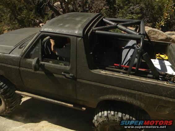 Dark green Ford Bronco with roll cage, off-road tires, and a driver visible