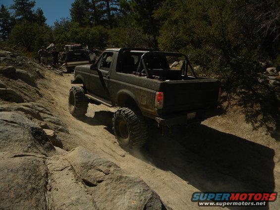 Dark 1992 Ford Bronco with roll cage and large tires on a rocky trail