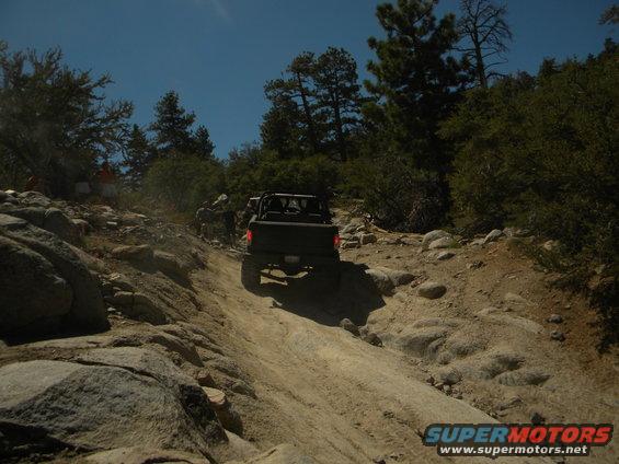 Off-road vehicle climbing a rocky trail with other vehicles and people visible