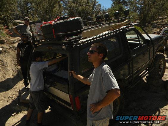 1992 Ford Bronco with roof rack and spare tire on a rocky trail, people loading gear