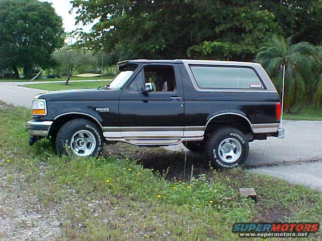 Black 1996 Ford Bronco with tan top parked on grassy shoulder