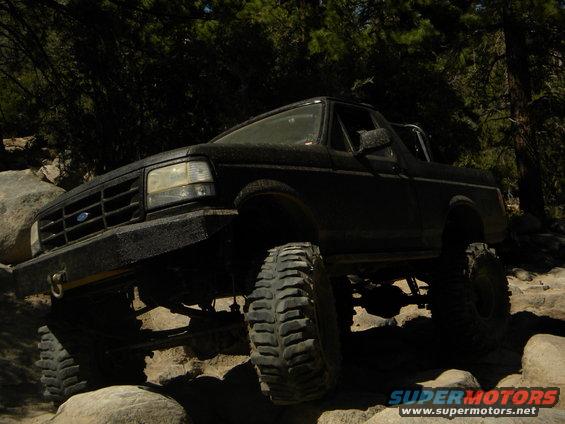 Black Ford Bronco with large tires climbing over rocks on a trail