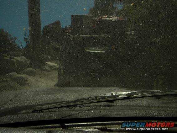 View from inside a dusty vehicle looking out at another off-road vehicle in a rocky, wooded area