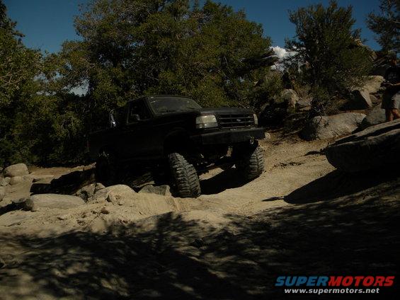 Black Ford F-Series truck driving over rocks on a dirt trail